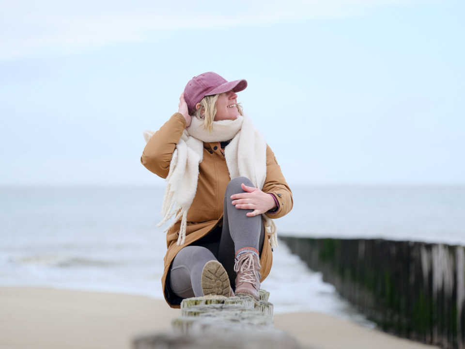 Alleine ans Meer im Winter – Frau sitzt entspannt am Strand und blickt auf die Nordsee
