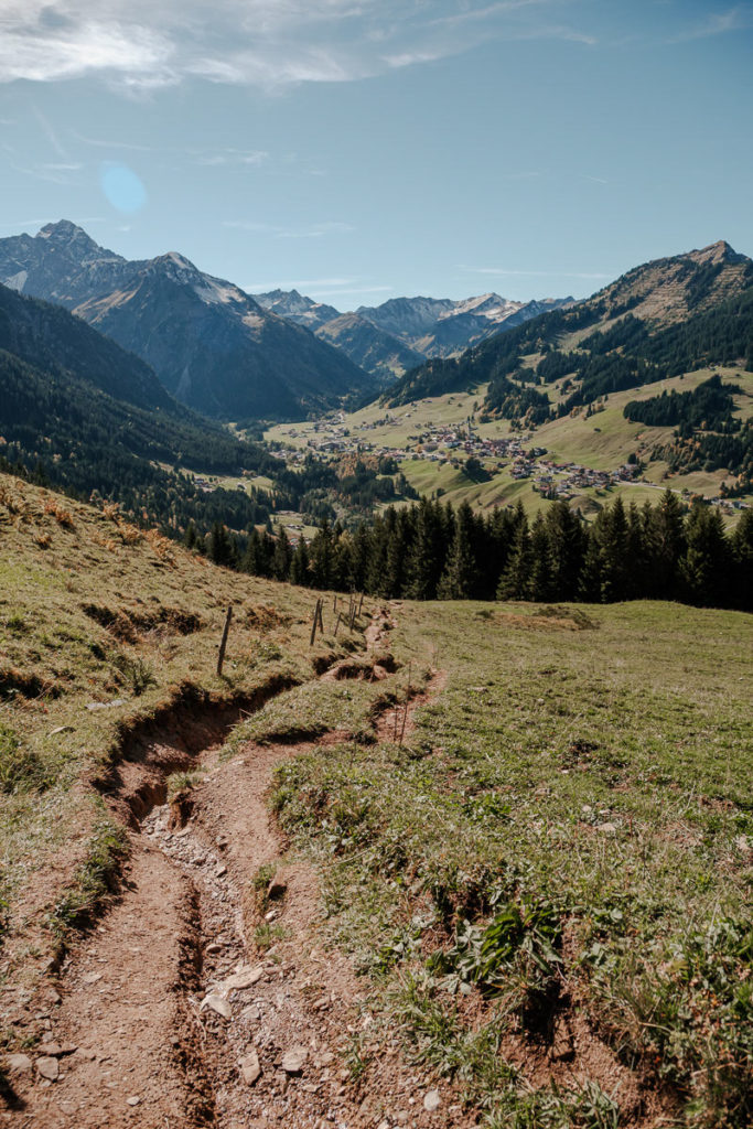Herbstliche Landschaft im Kleinwalsertal mit bunten Wäldern und Bergen bei einer Wanderung von der Alpe Kuhgehren zurück ins Tal.