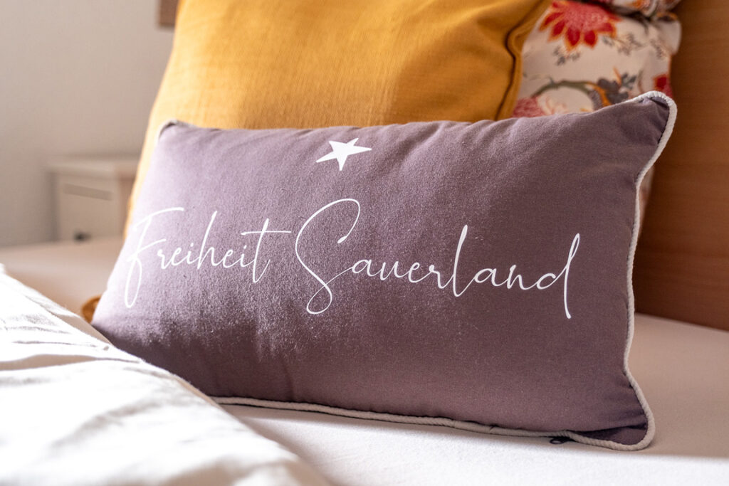 Graues Dekokissen mit Schriftzug „Freiheit Sauerland“ auf dem Bett