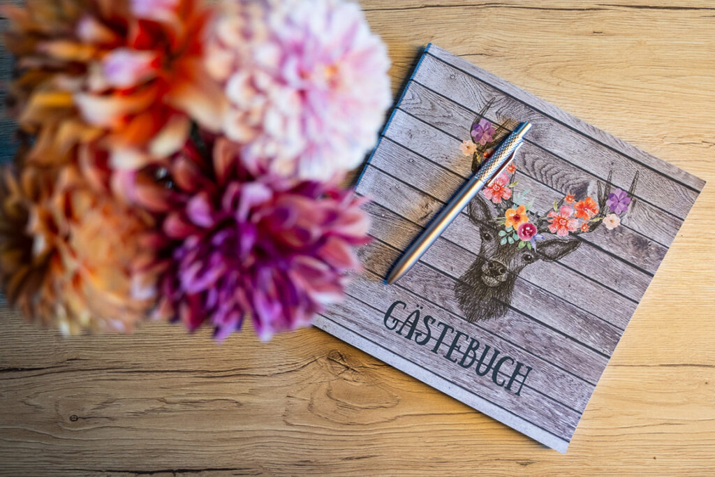 Gästebuch mit Stift und Blumen auf einem Holztisch